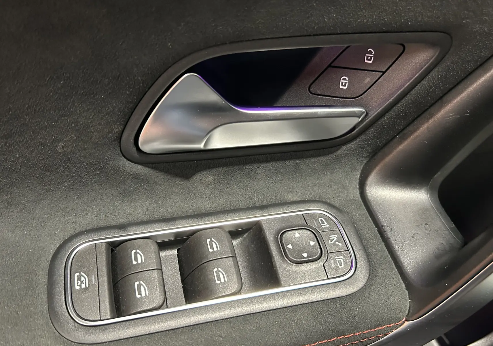 Gros plan sur la poignée intérieure et les commandes des vitres côté conducteur d'une Mercedes CLA Shooting Brake noir métallisé.