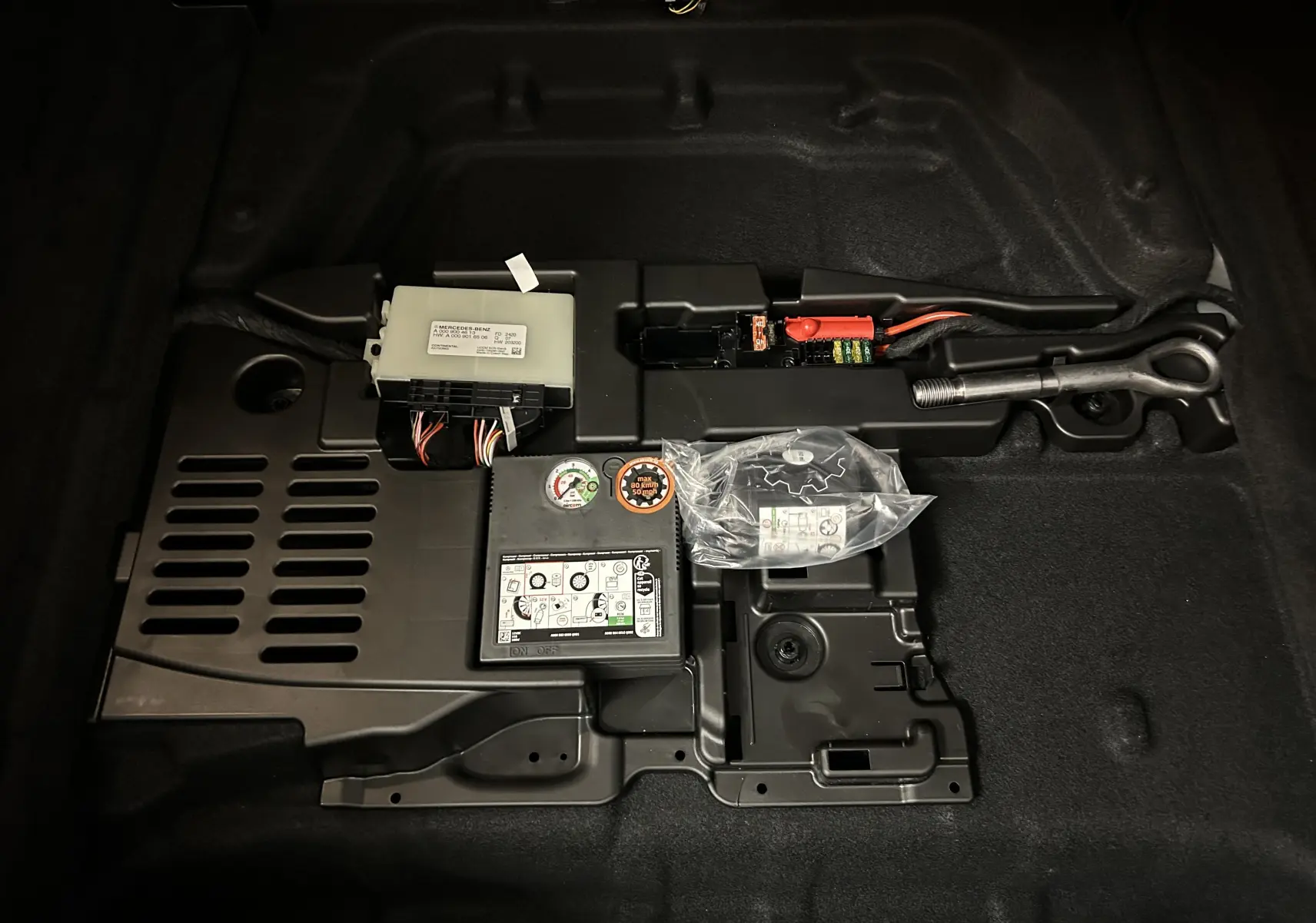 Vue rapprochée du compartiment de rangement sous le coffre d'une Mercedes CLA Shooting Brake noire, montrant outils et kit de réparation.