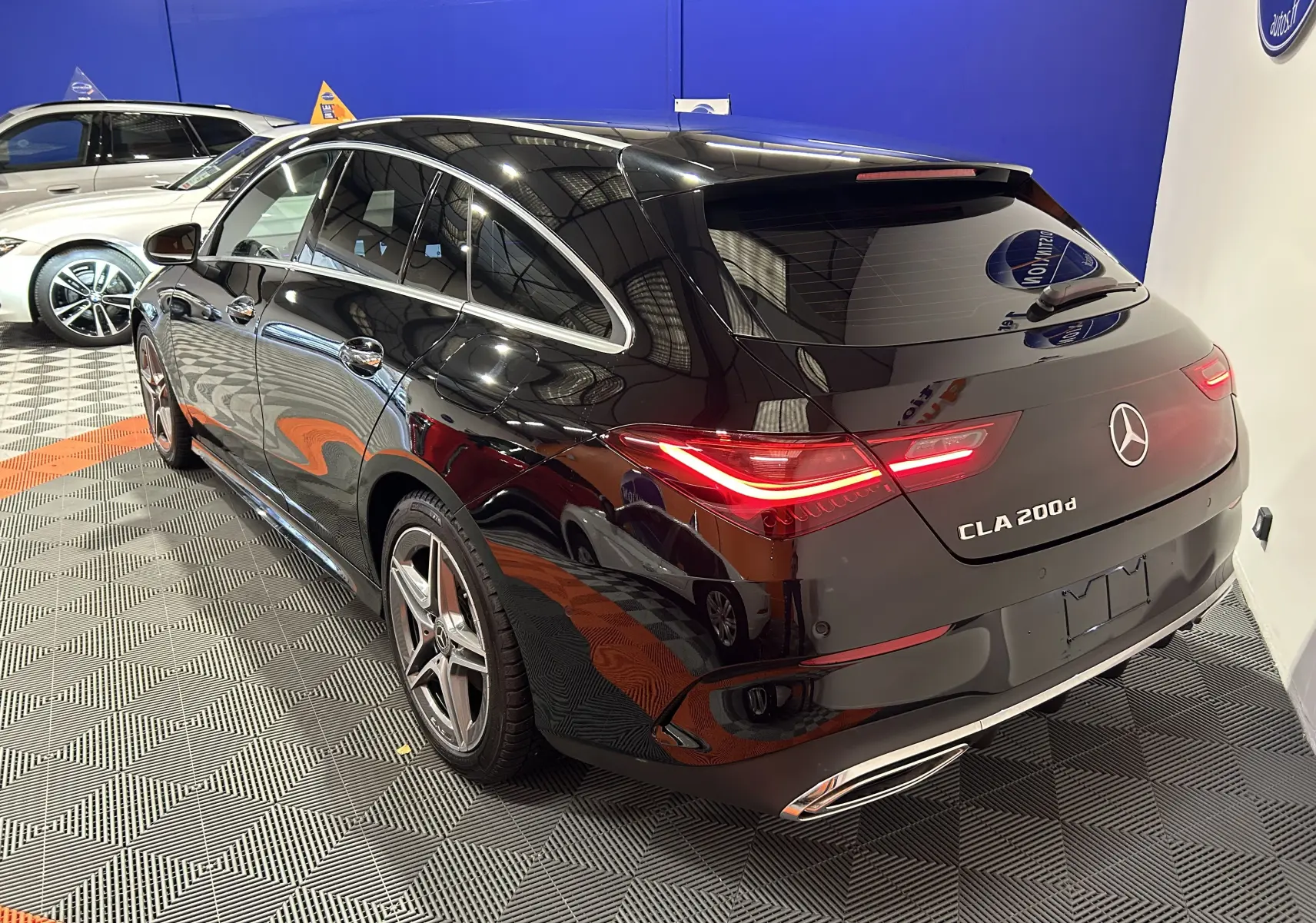 Mercedes Classe CLA Shooting Brake noir métallisé vue 3/4 arrière droit avec feux LED allumés en intérieur showroom.