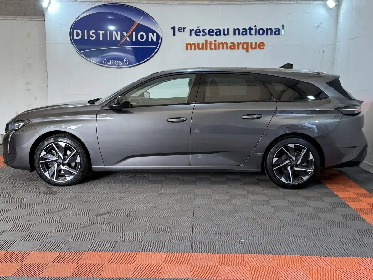 Profil droit d'une Peugeot 308 SW gris foncé 2022, avec jantes alliage et toit noir, stationnée en intérieur showroom.