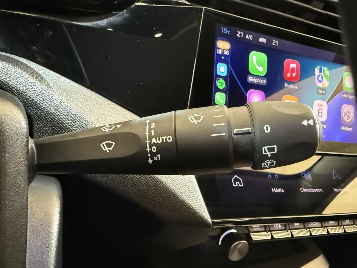 Gros plan sur la commande des essuie-glaces à gauche du volant, avec écran tactile affichant les applications du système multimédia.