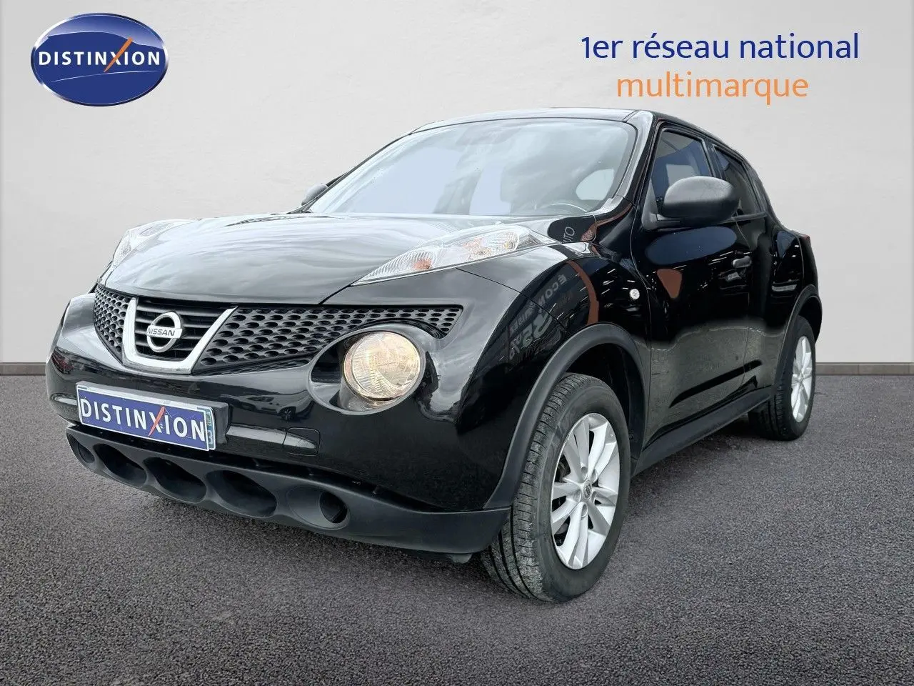 Nissan Juke noir en 3/4 avant droit, avec phares ronds allumés et jantes argentées visibles.