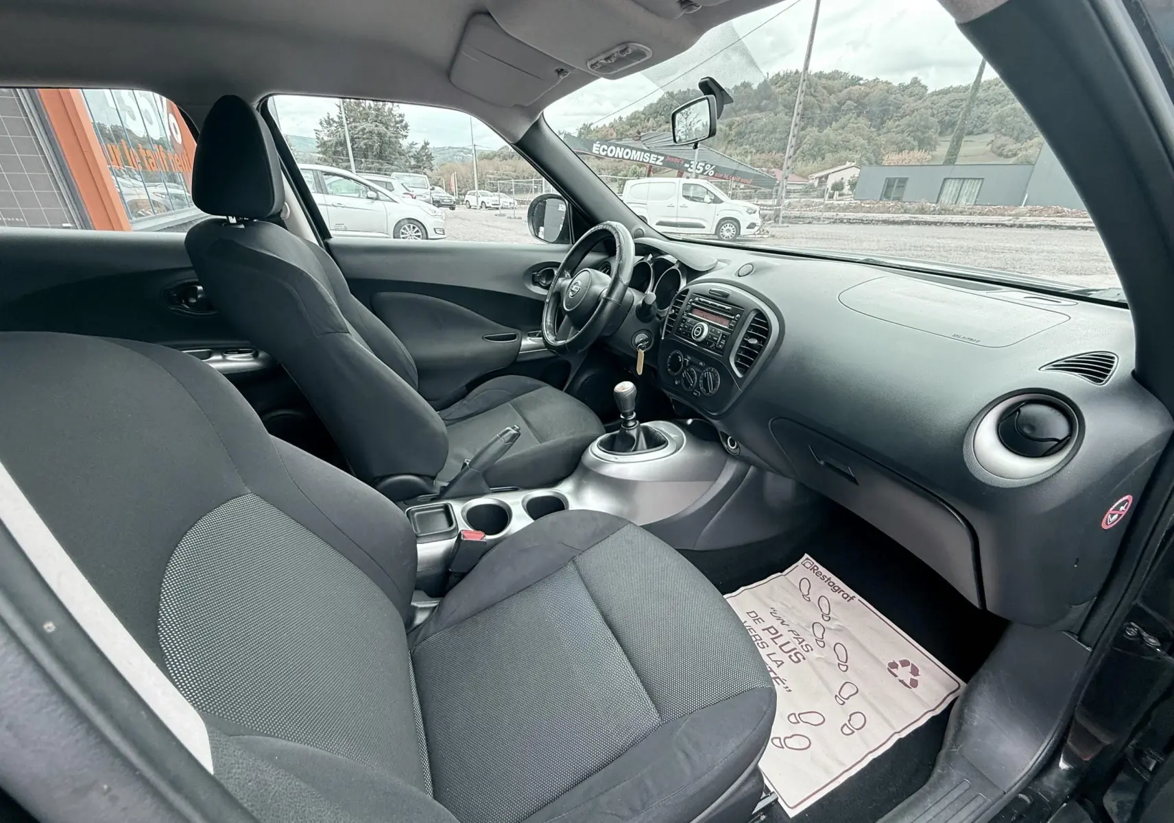 Intérieur noir du Nissan Juke 2012 vu côté passager, montrant sièges en tissu et tableau de bord avec boîte manuelle.