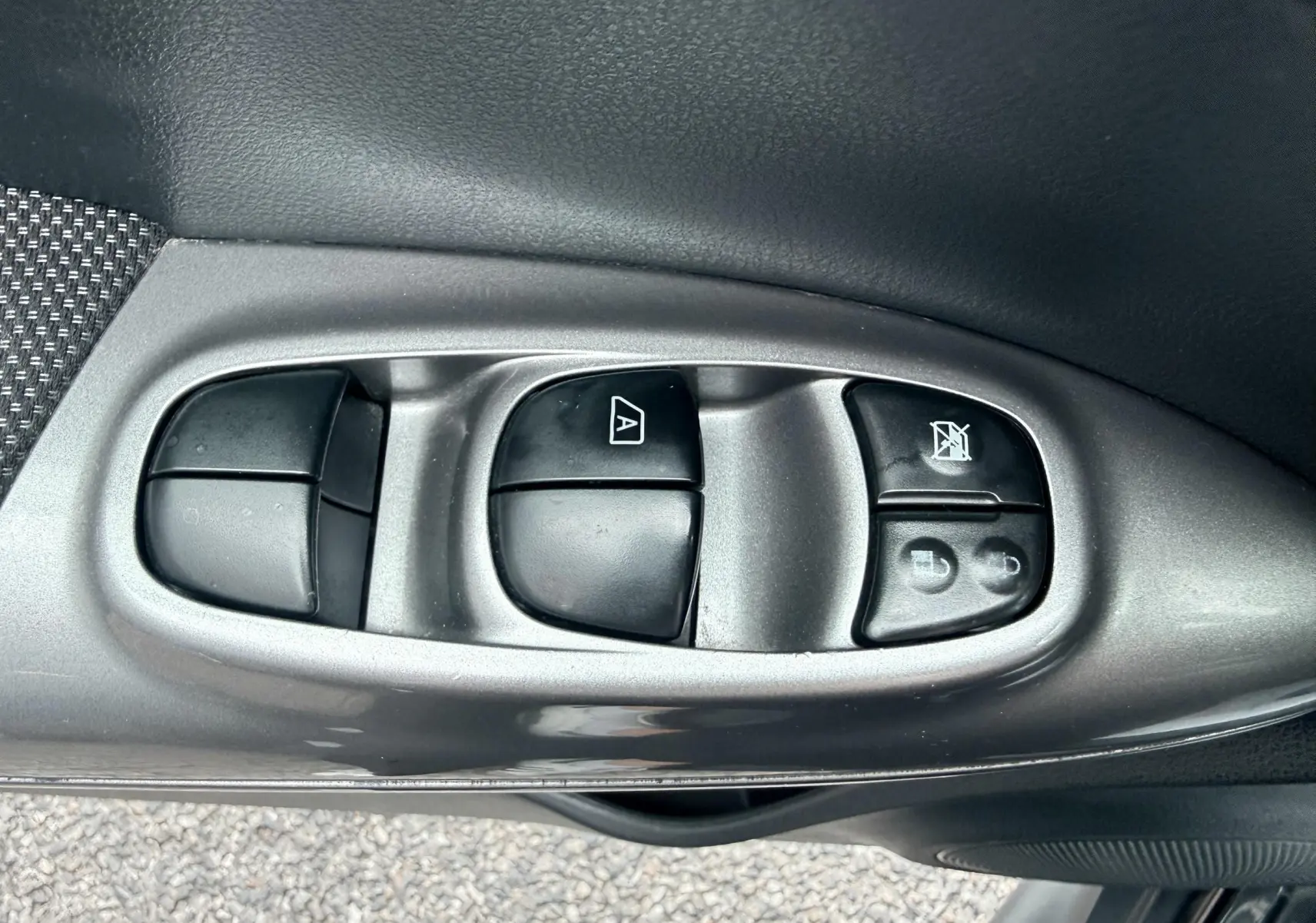 Gros plan sur les commandes des vitres électriques côté conducteur d’un Nissan Juke noir de 2012.