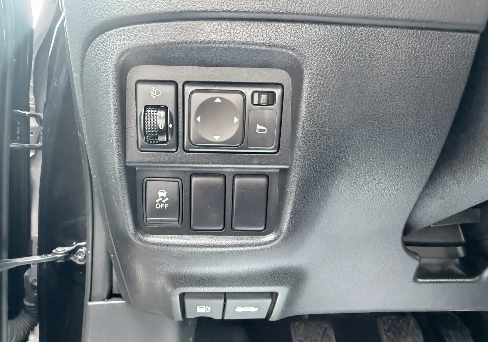 Vue rapprochée des commandes côté gauche du tableau de bord noir du Nissan Juke 2012, avec boutons de réglage des phares et rétroviseurs.