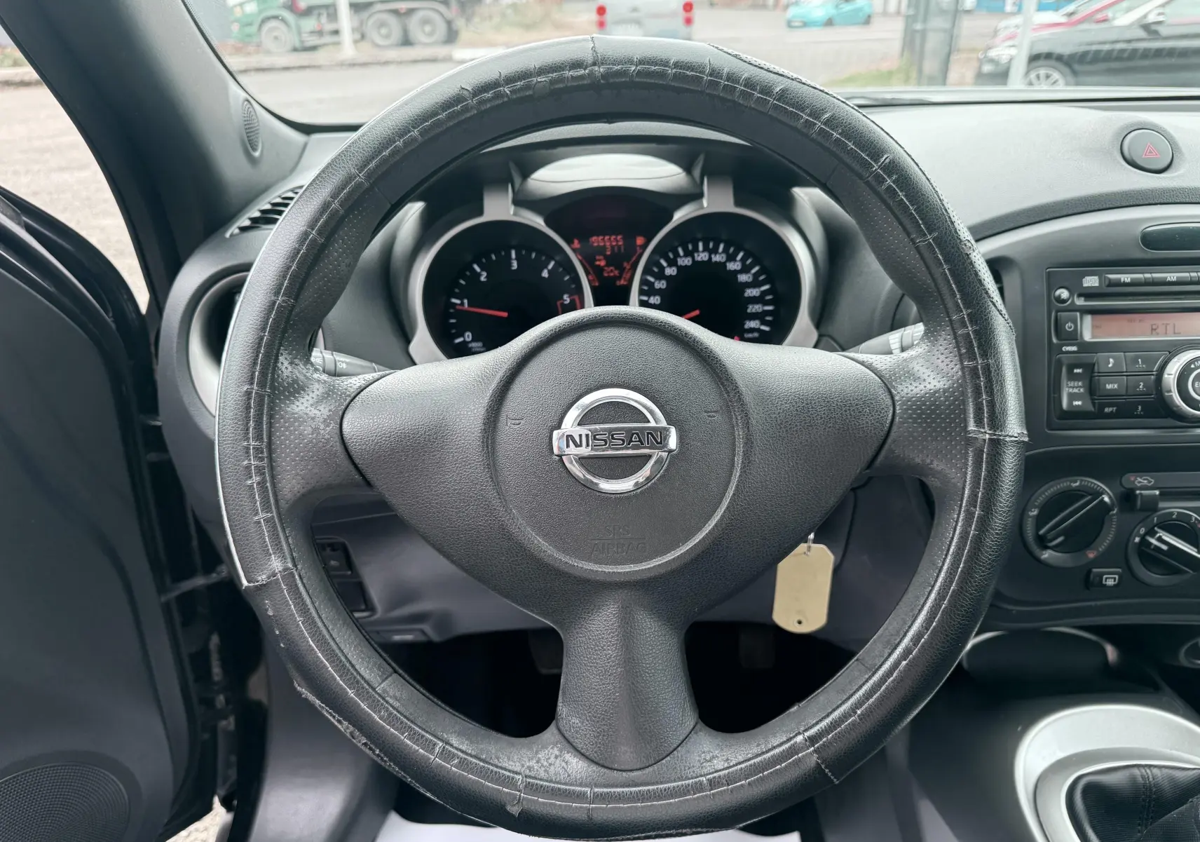 Vue centrée sur le volant noir usé d’un Nissan Juke 2012, avec tableau de bord et console radio visibles.