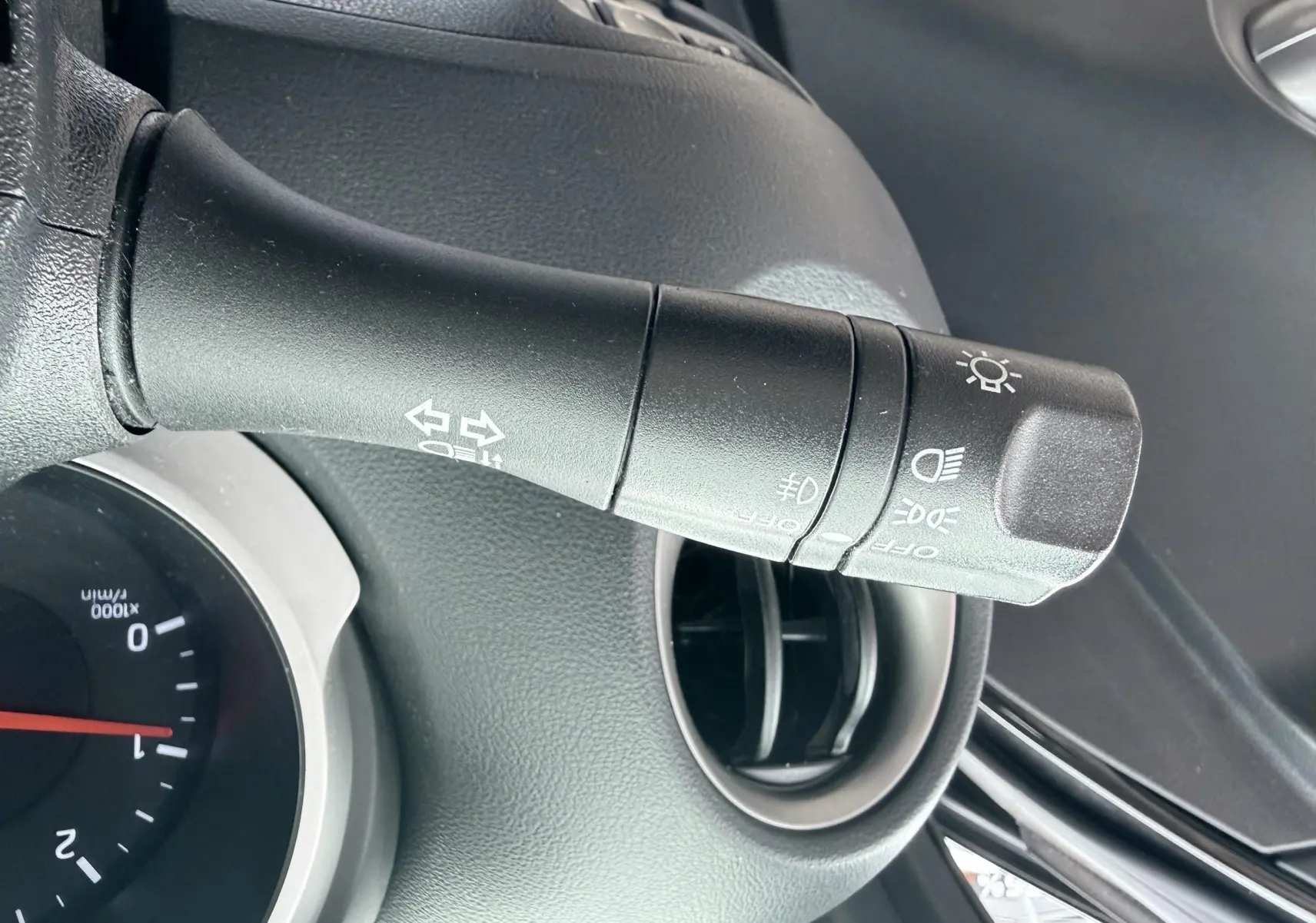 Gros plan sur la commande des phares et clignotants dans l’habitacle noir d’un Nissan Juke 2012.