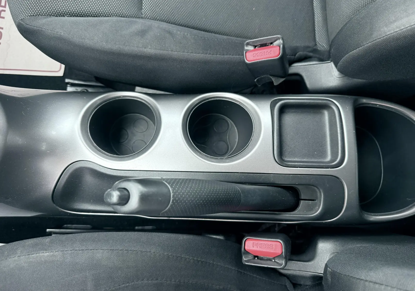 Vue plongeante sur la console centrale noire du Nissan Juke 2012, avec frein à main, porte-gobelets et ceintures de sécurité.