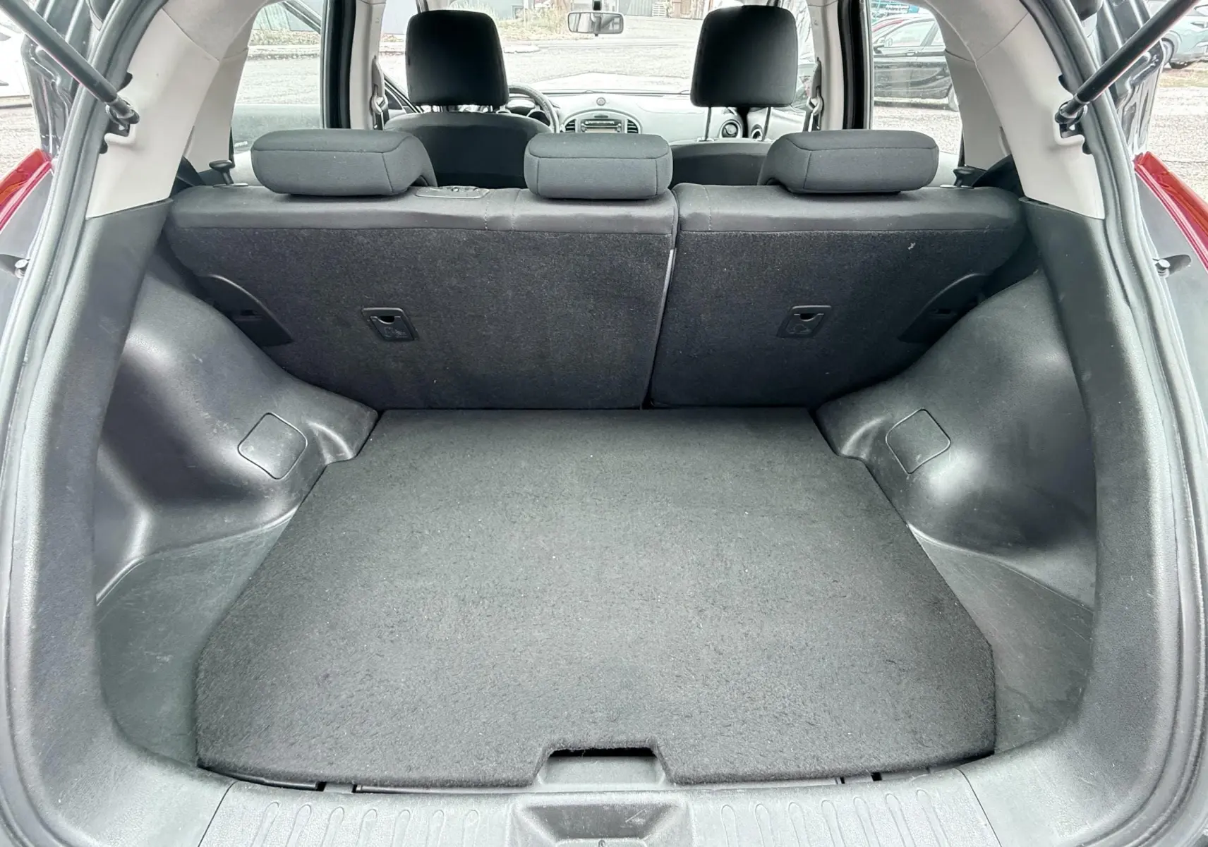 Vue du coffre ouvert d'un Nissan Juke noir 2012, montrant l'espace de chargement et les dossiers des sièges arrière en tissu noir.