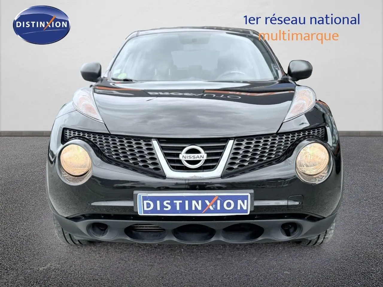 Vue frontale d'un Nissan Juke noir de 2012 avec phares allumés et calandre distinctive en nid d'abeille.