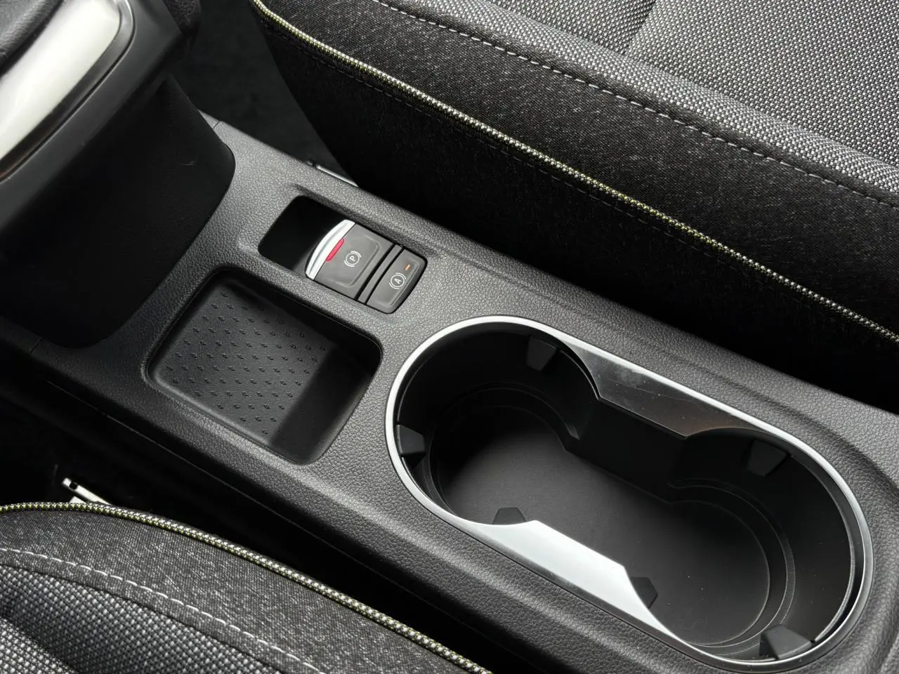 Gros plan sur la console centrale noire étoile du Renault Captur 2025, avec porte-gobelets et frein à main électrique.