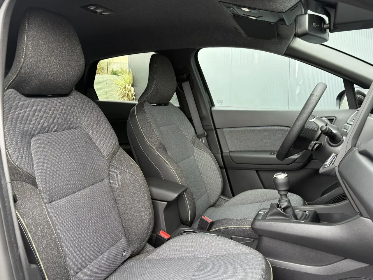 Vue intérieure côté gauche du Renault Captur 2025, sièges gris texturés et volant avec levier de vitesses manuel.