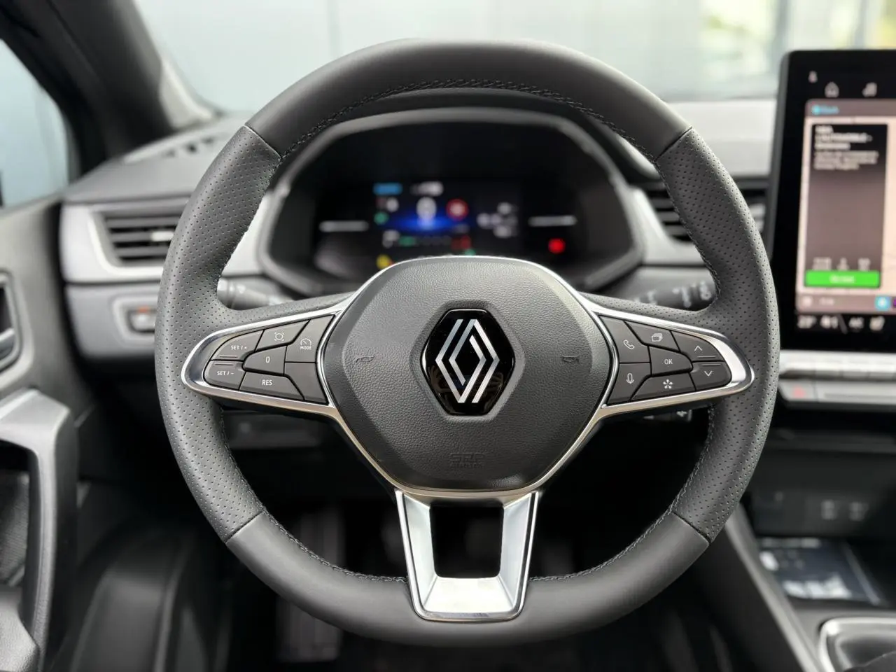 Volant en cuir perforé avec logo Renault, vue frontale centrée sur le tableau de bord numérique et écran tactile latéral.
