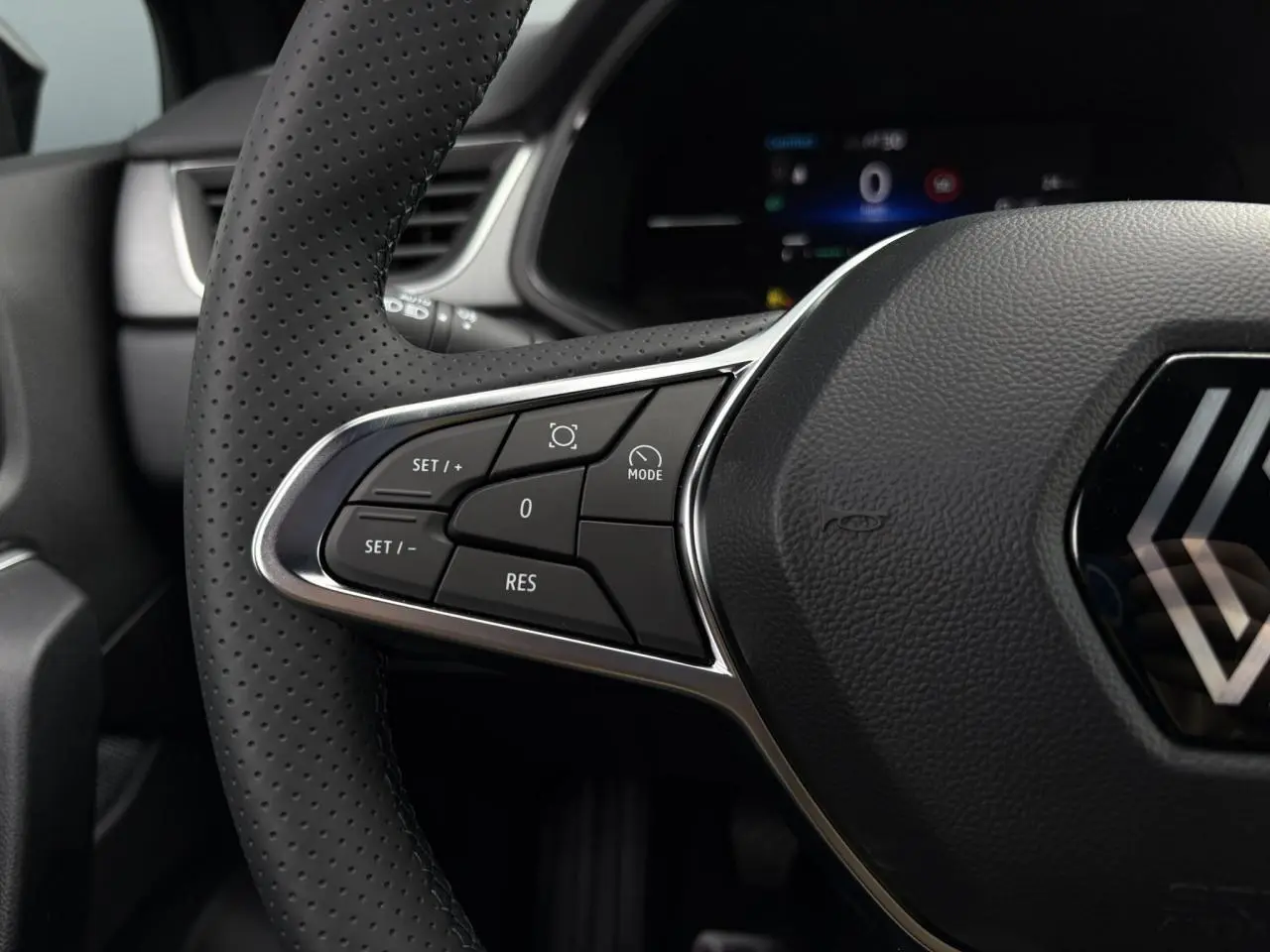 Gros plan sur le volant perforé noir du Renault Captur 2025 avec commandes intégrées et logo central chromé.