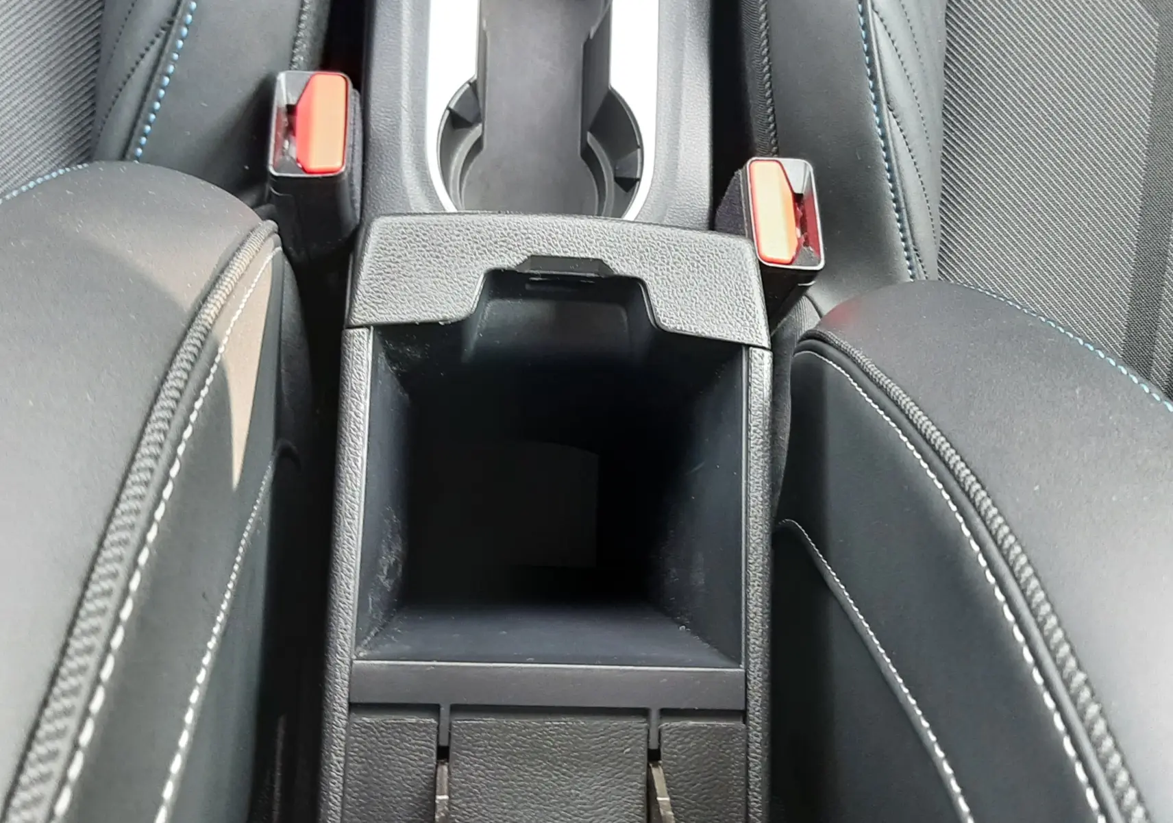 Vue plongeante sur la console centrale noire du Renault Captur 2024, avec porte-gobelets et accoudoirs en tissu noir.