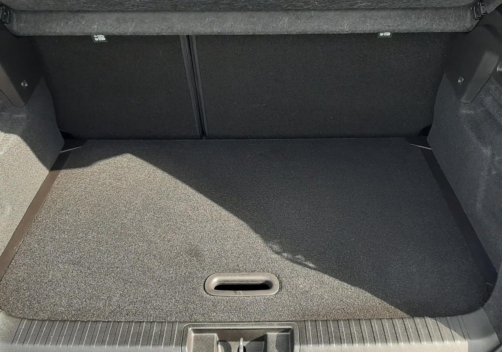 Coffre ouvert vu de l'arrière du Renault Captur 2024 bleu iron avec intérieur noir et tapis de coffre gris.