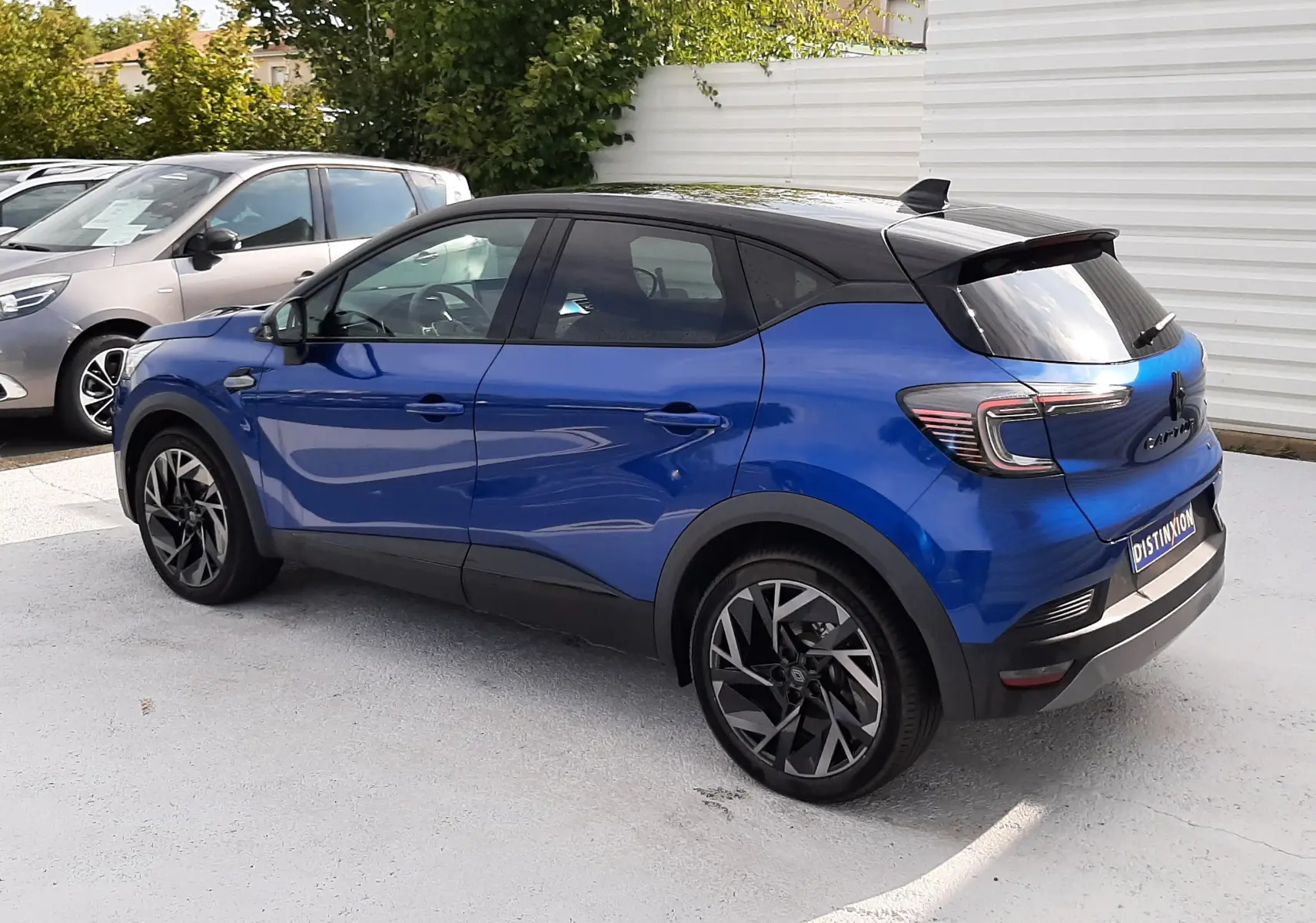 Vue 3/4 arrière droite d'un Renault Captur 2024 bleu Iron avec toit noir et jantes alliage noires.