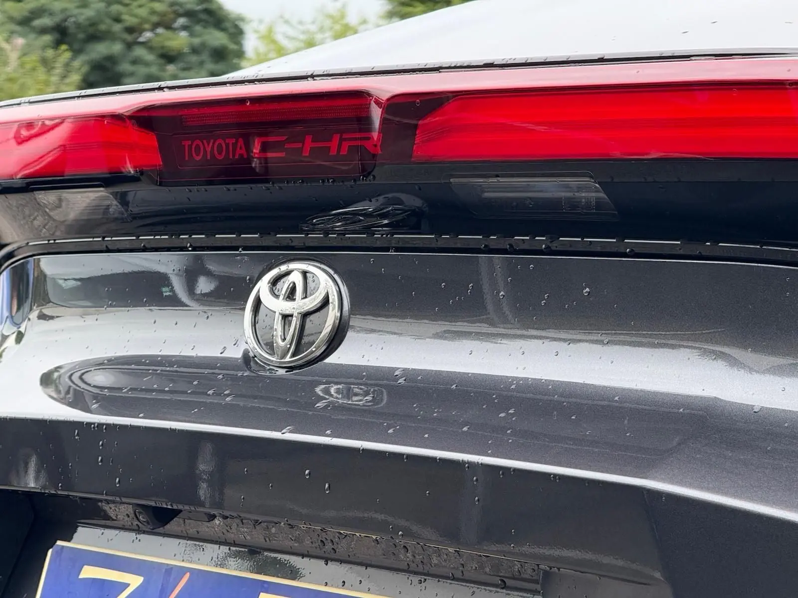 Gros plan arrière sur le hayon gris atlas du Toyota C-HR 1.8 140CH STYLE MY25 avec logo et feu stop rouge intégré.