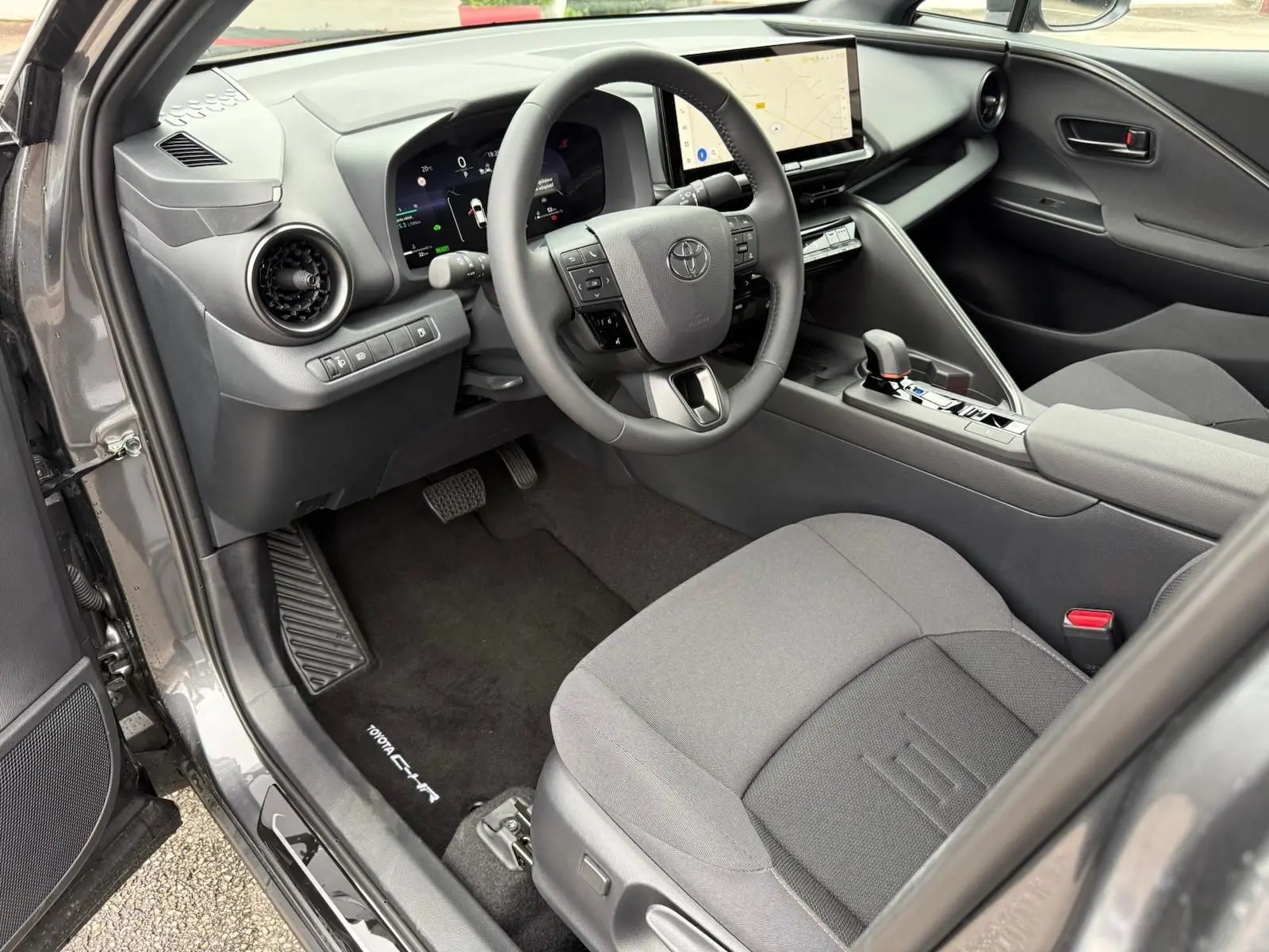Intérieur avant gauche du Toyota C-HR gris atlas 2025, volant multifonction et écran tactile central visible.
