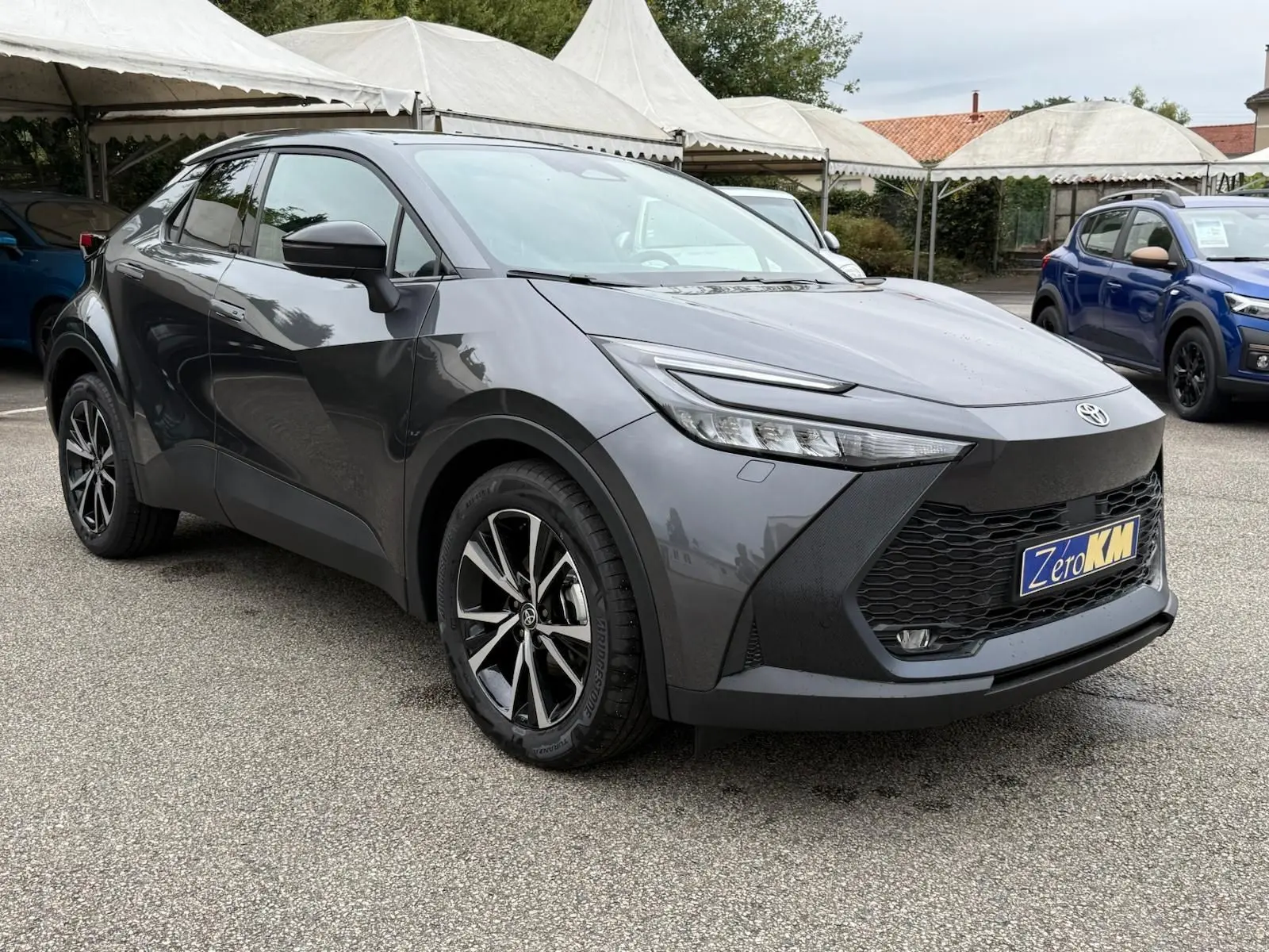 Toyota C-HR 1.8 140CH STYLE gris atlas en 3/4 avant droit, avec jantes alliage et calandre noire distinctive.