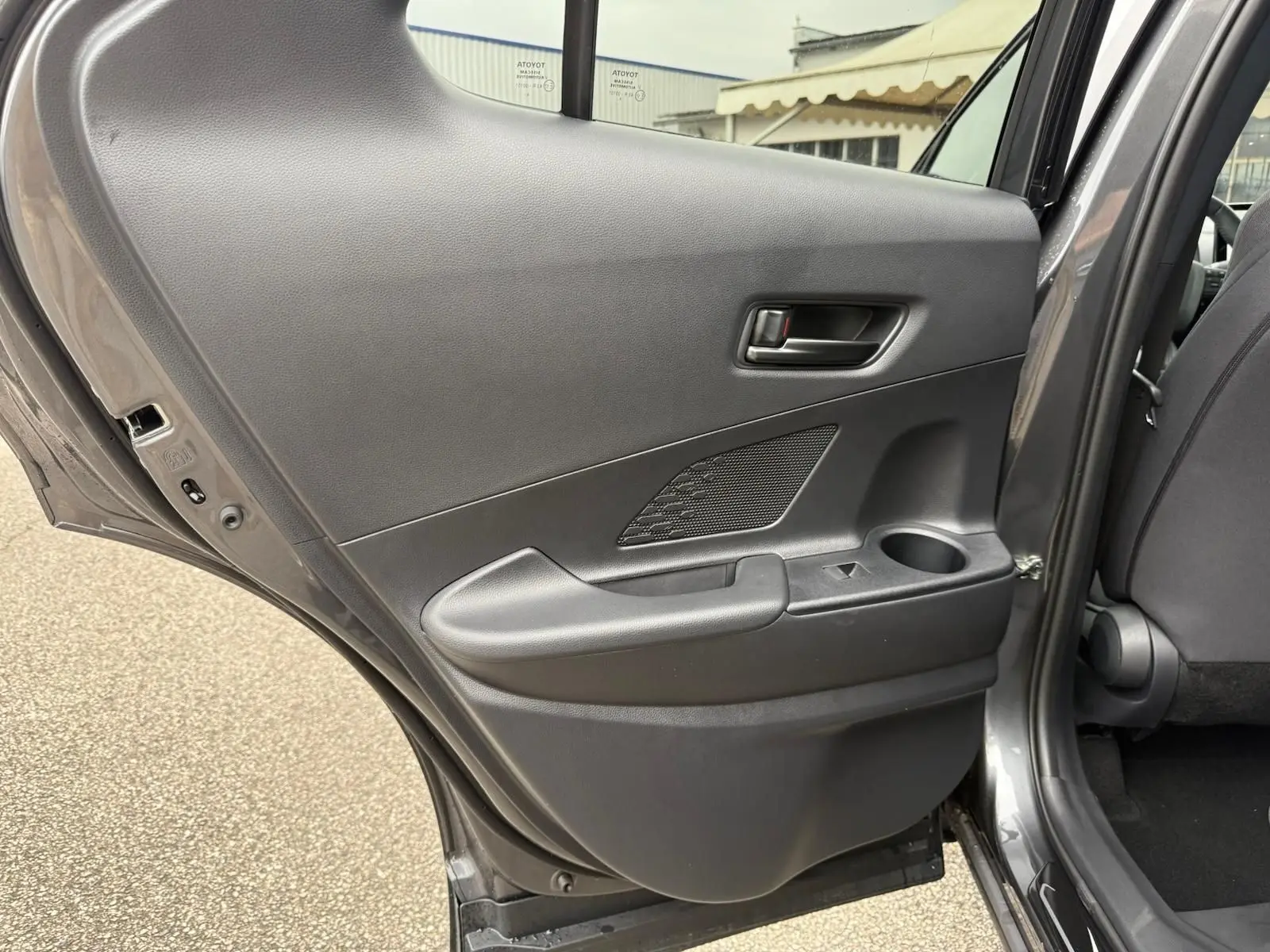 Vue intérieure de la porte arrière gauche gris atlas du Toyota C-HR 1.8 140CH STYLE MY25 avec accoudoir et porte-gobelet intégré.