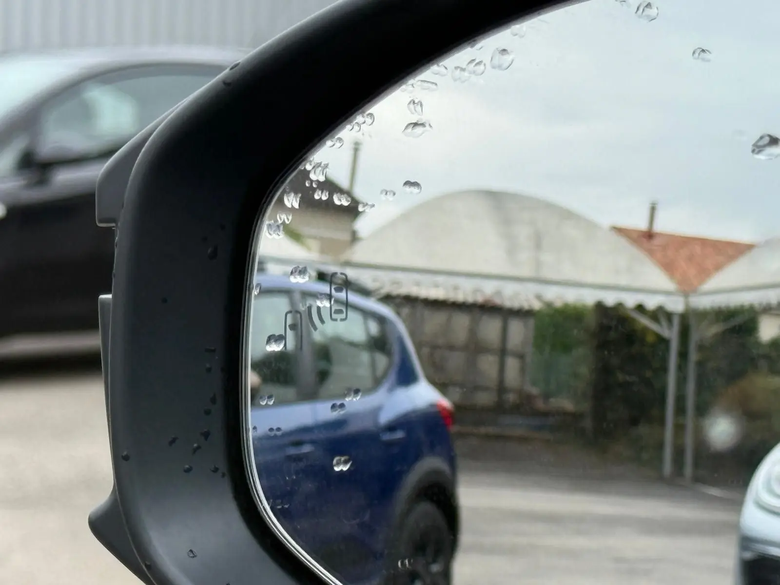 Reflet dans le rétroviseur montrant un SUV bleu en stationnement, avec gouttes de pluie sur le miroir.