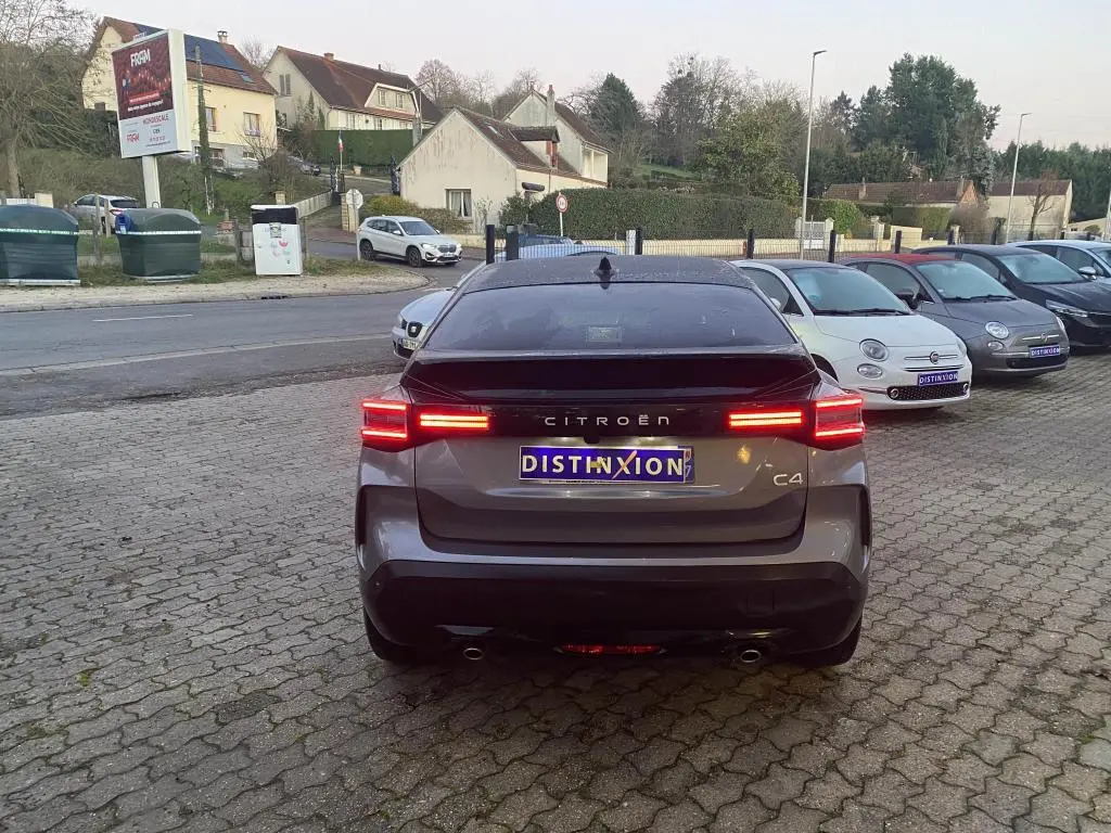 Vue arrière d'une Citroën C4 gris foncé avec toit noir, feux arrière LED allumés sur parking pavé.