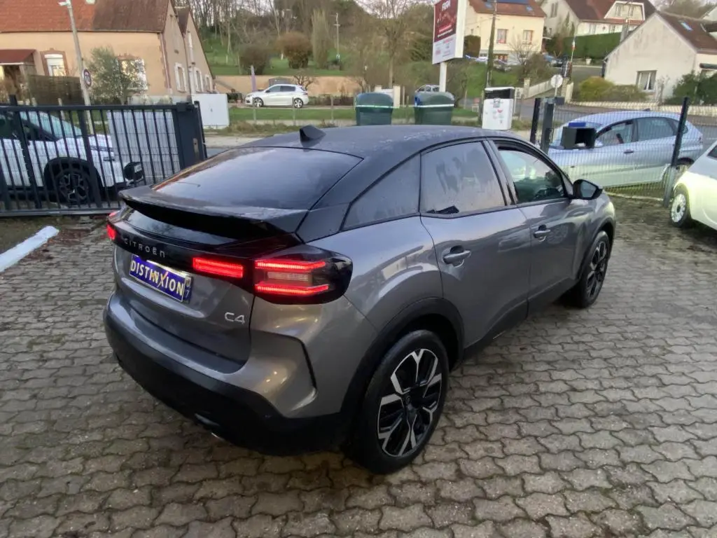 Vue 3/4 arrière droite d'une Citroën C4 2025 gris foncé avec toit noir et feux arrière LED allumés.