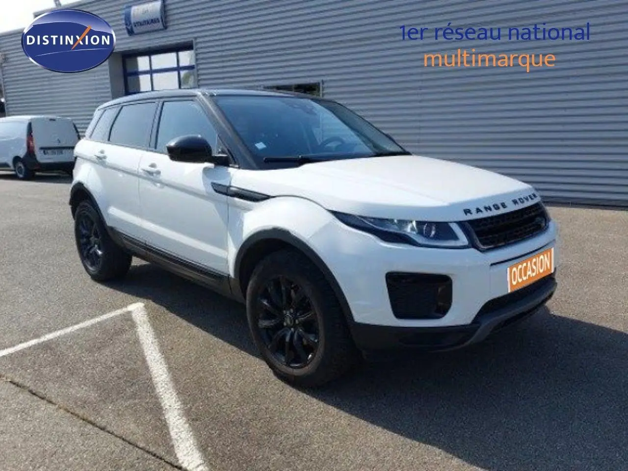 Range Rover Evoque blanc en 3/4 avant droit avec jantes noires, stationné devant un bâtiment industriel.
