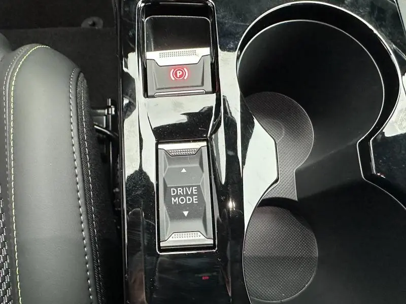 Gros plan sur la console centrale noire brillante de la Peugeot 208 Hybrid avec bouton Drive Mode et frein à main électronique.