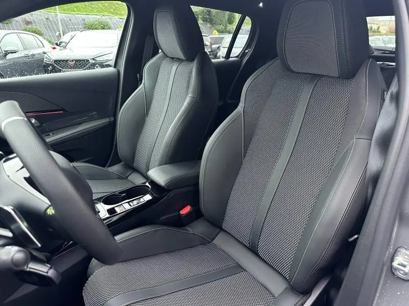 Intérieur de la Peugeot 208 1.2 Hybrid 110ch GT 2025, vue côté conducteur, sièges tissu et cuir gris avec surpiqûres vertes.