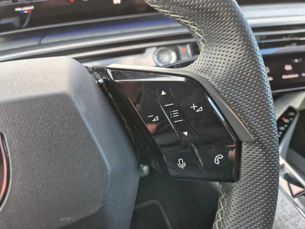 Gros plan sur le côté droit du volant perforé du Peugeot 3008 Hybrid 136 e-DCS6 GT gris clair, avec commandes vocales et appels.