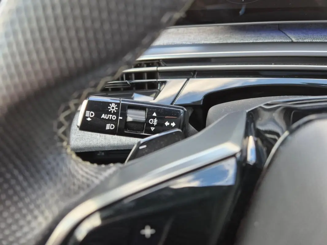 Gros plan sur la commande d’allumage automatique des feux derrière le volant du Peugeot 3008 Hybrid gris clair 2024.