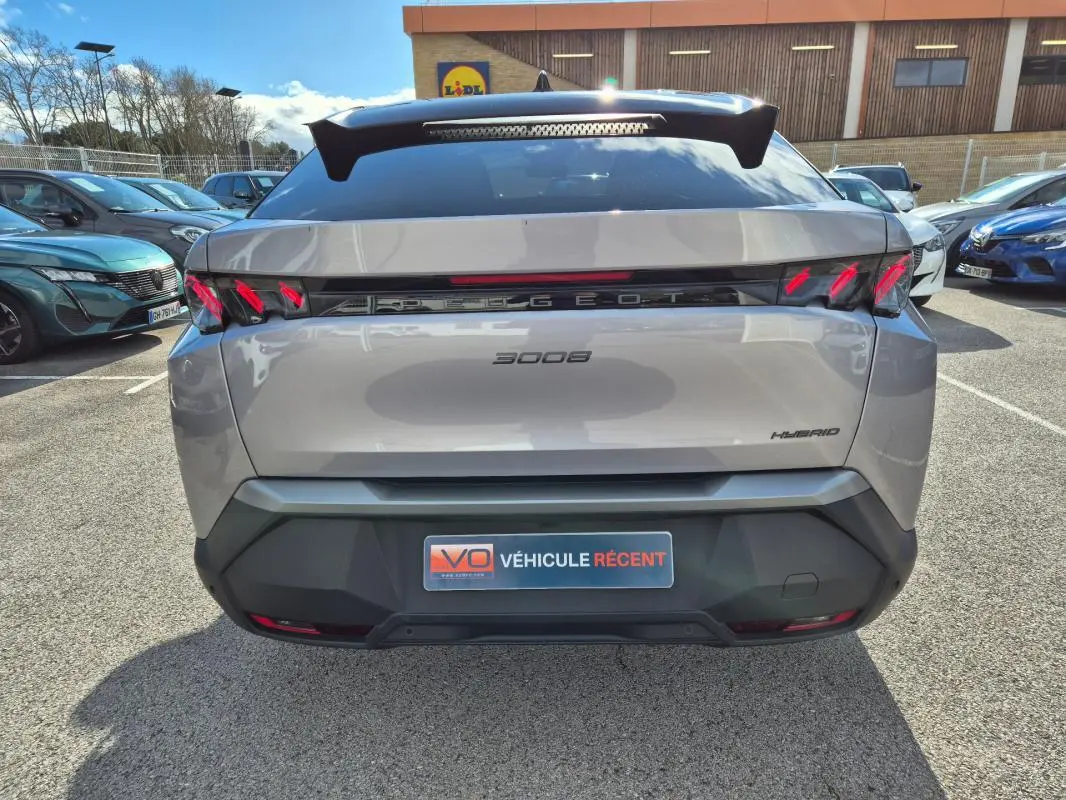 Vue arrière d’un Peugeot 3008 Hybrid gris clair 2024 avec feux arrière LED et logo Peugeot lumineux.