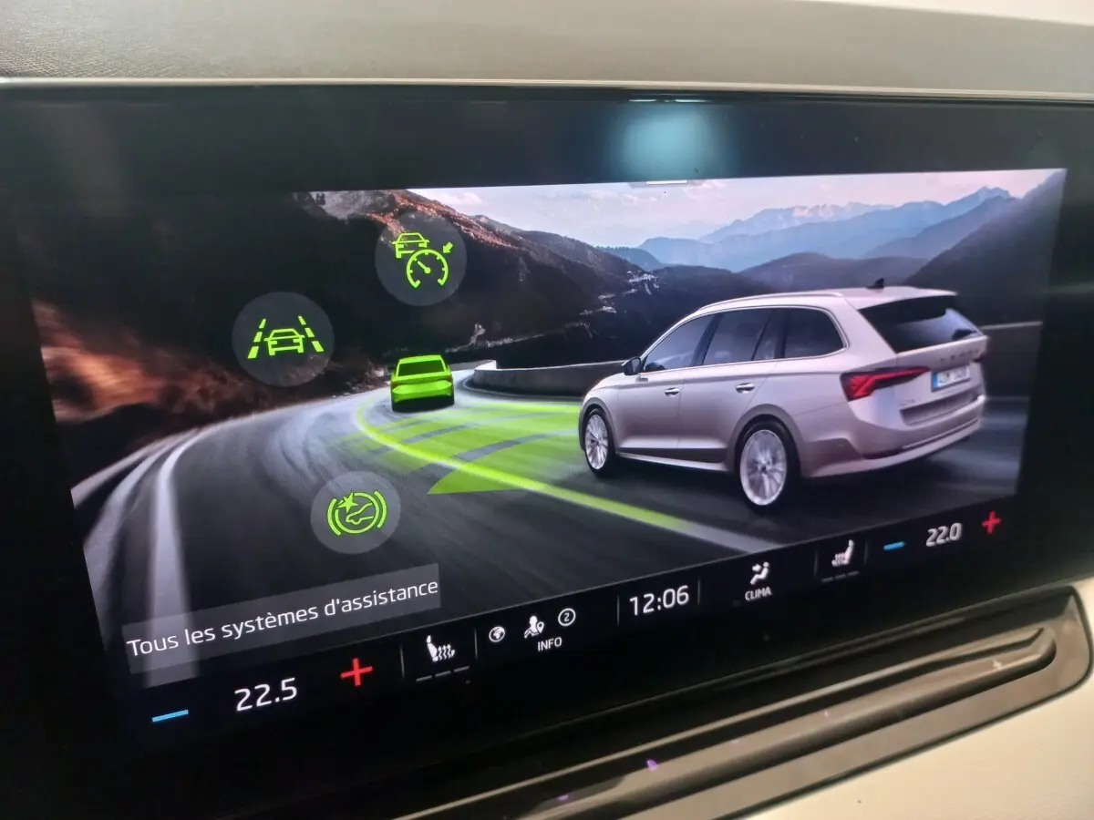 Affichage tactile montrant une Skoda Octavia beige vue de trois quarts arrière sur route de montagne sinueuse.