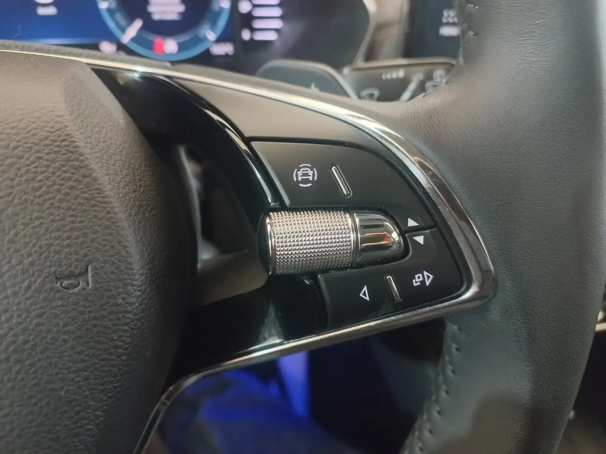 Gros plan sur les commandes multifonctions en alu et cuir du volant de la Skoda Octavia bleu, tableau de bord numérique en arrière-plan.