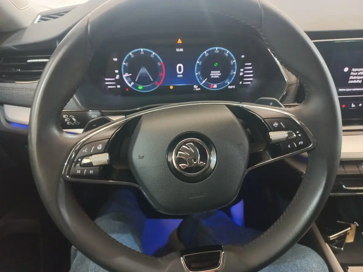 Vue rapprochée du volant cuir noir de la Skoda Octavia 2022 avec tableau de bord numérique et éclairage d’ambiance bleu.