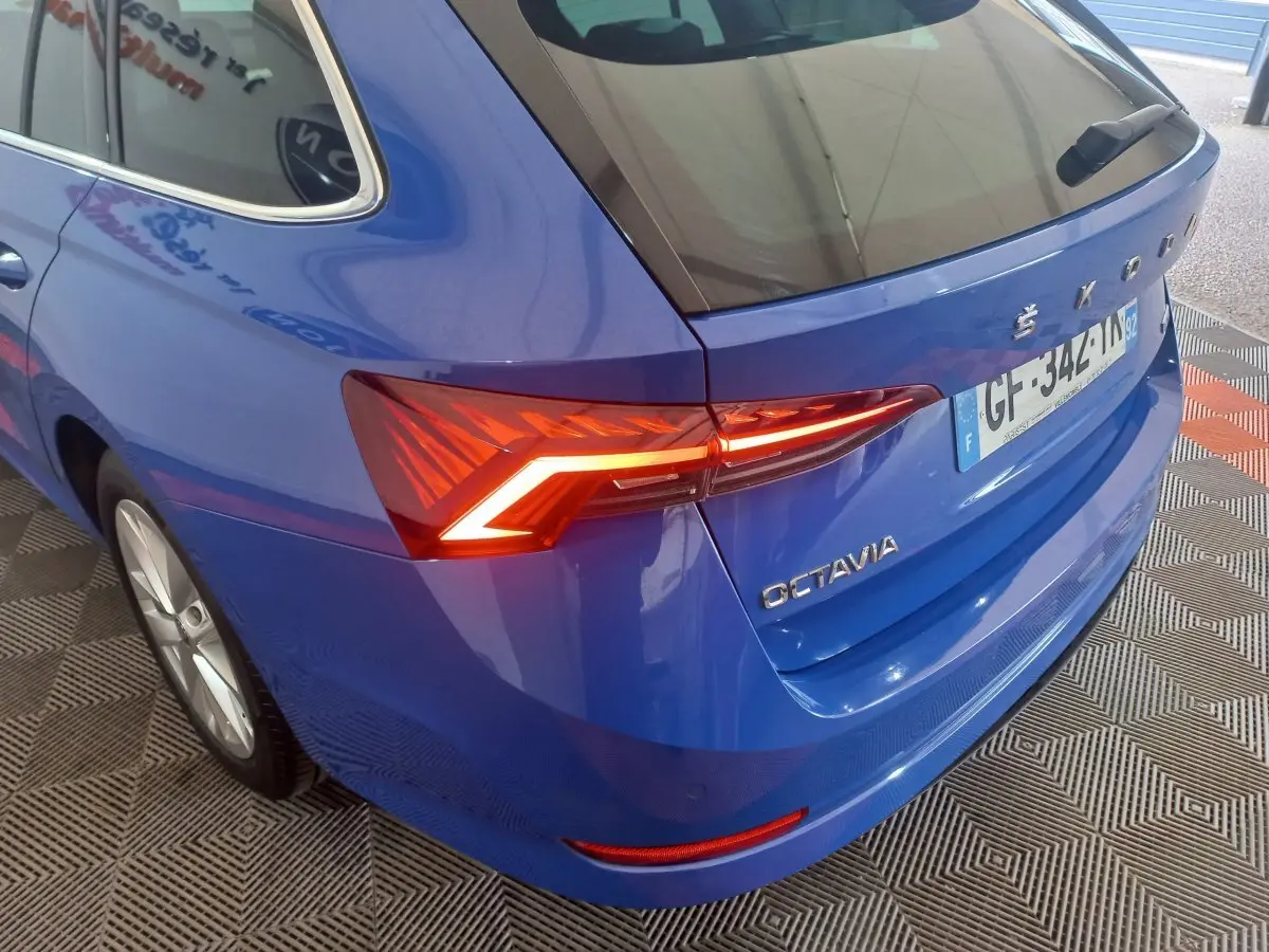 Vue 3/4 arrière droite d'une Skoda Octavia bleue 2022 avec feux arrière LED allumés et logo visible.