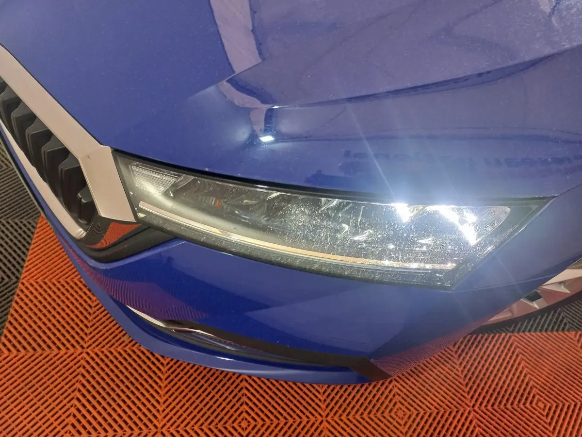 Gros plan sur le phare avant droit et la calandre d'une Skoda Octavia bleu électrique, vue en légère plongée.