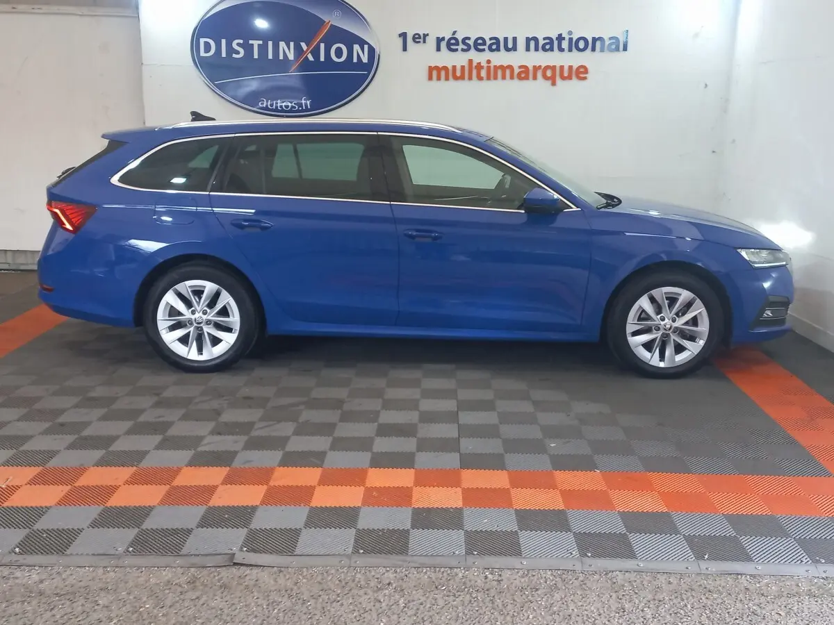 Vue latérale droite d'une Skoda Octavia break bleu 2022 dans un showroom avec sol à damiers gris et orange.