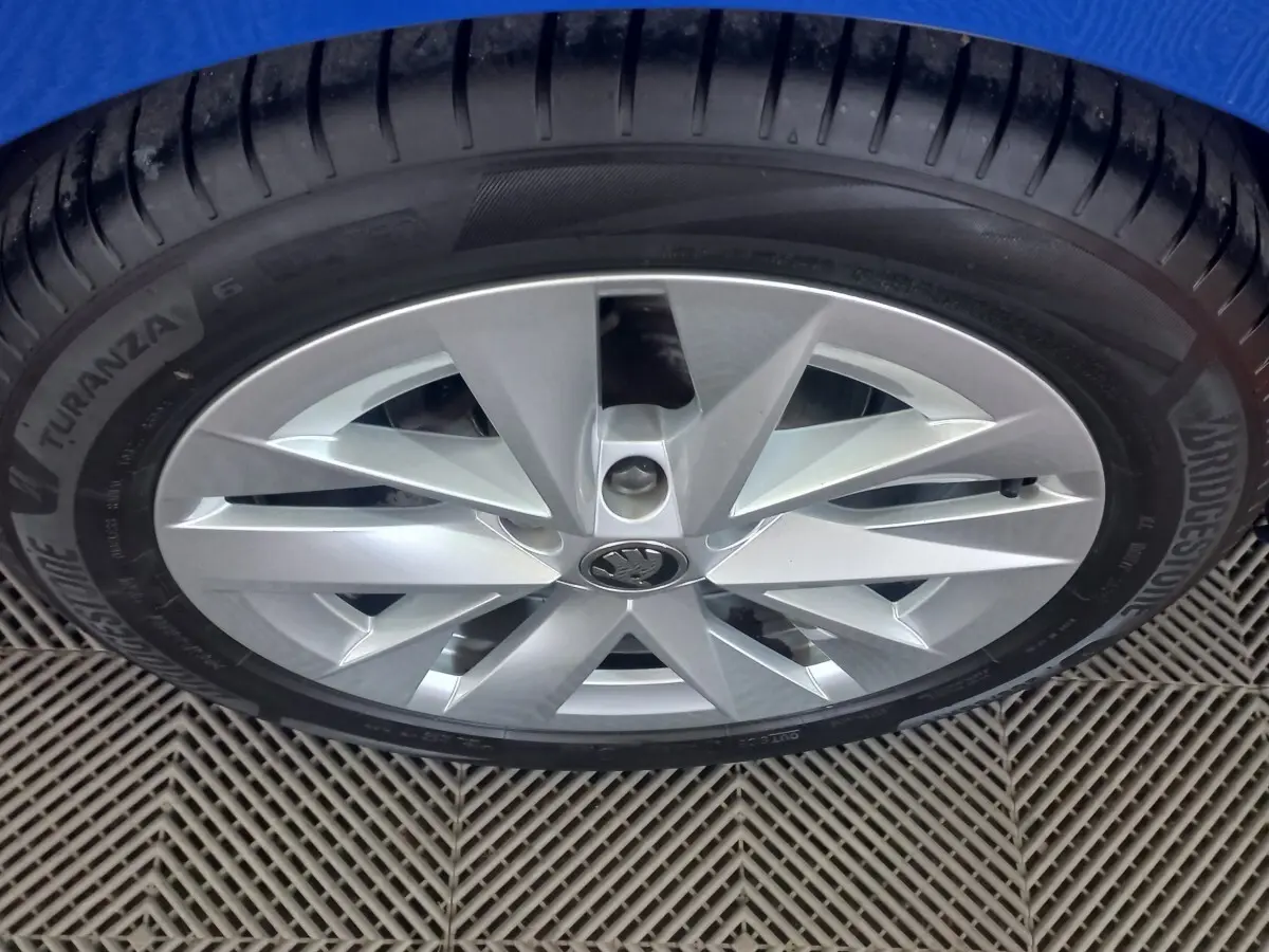 Gros plan sur la roue avant droite avec jante argentée et logo ŠKODA au centre sur fond bleu.