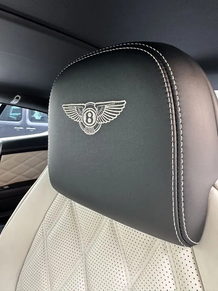 Gros plan sur l'appui-tête noir brodé du logo Bentley avec surpiqûres blanches, siège cuir beige perforé intérieur Continental GT.