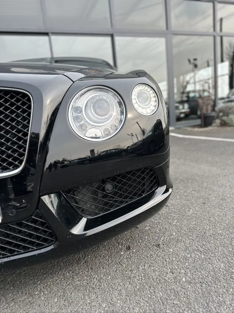 Gros plan sur le phare avant droit noir brillant d'une Bentley Continental GT 4.0 V8 Mulliner 2013, avec calandre en nid d'abeille.