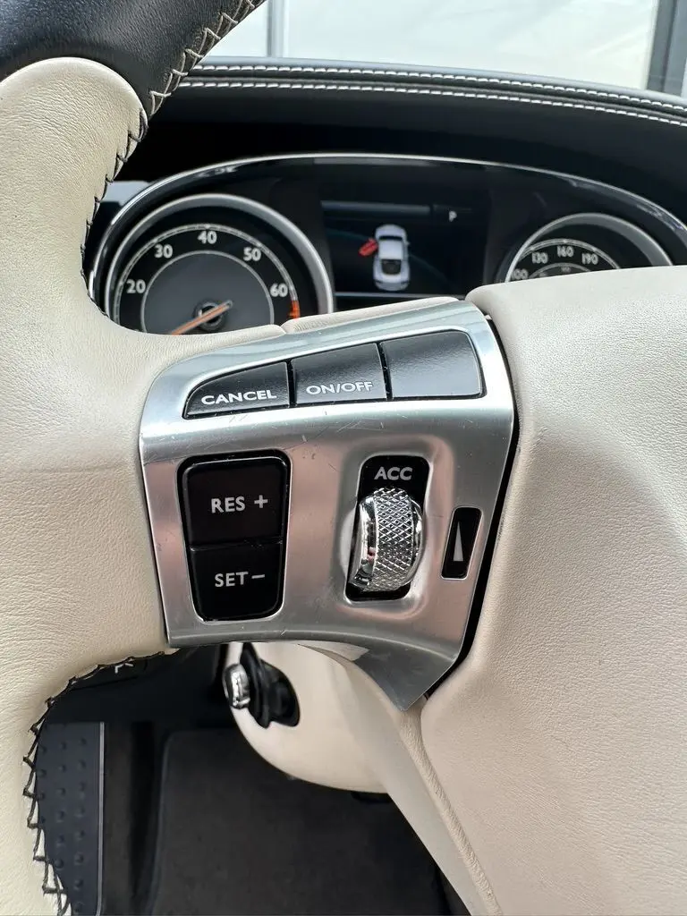 Gros plan sur les commandes de régulateur de vitesse sur le volant cuir beige de la Bentley Continental GT noire 2013.