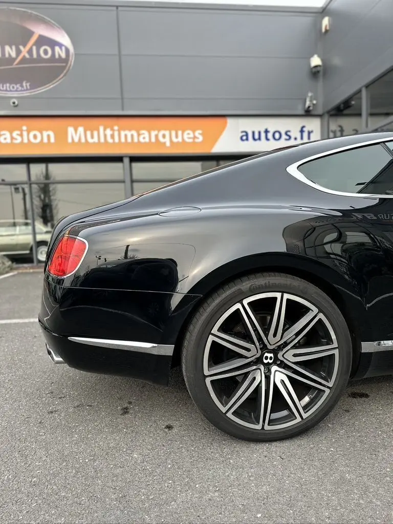Vue arrière côté gauche d'une Bentley Continental GT Mulliner noire, mettant en valeur la jante distinctive et la ligne fluide du coffre.