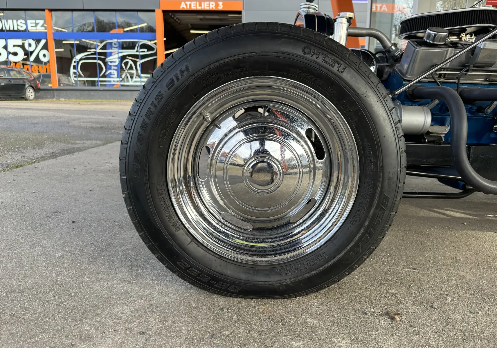Gros plan sur la roue chromée avant droite du Ford T Hot Rod noir de 1923, moteur V8 visible en arrière-plan.