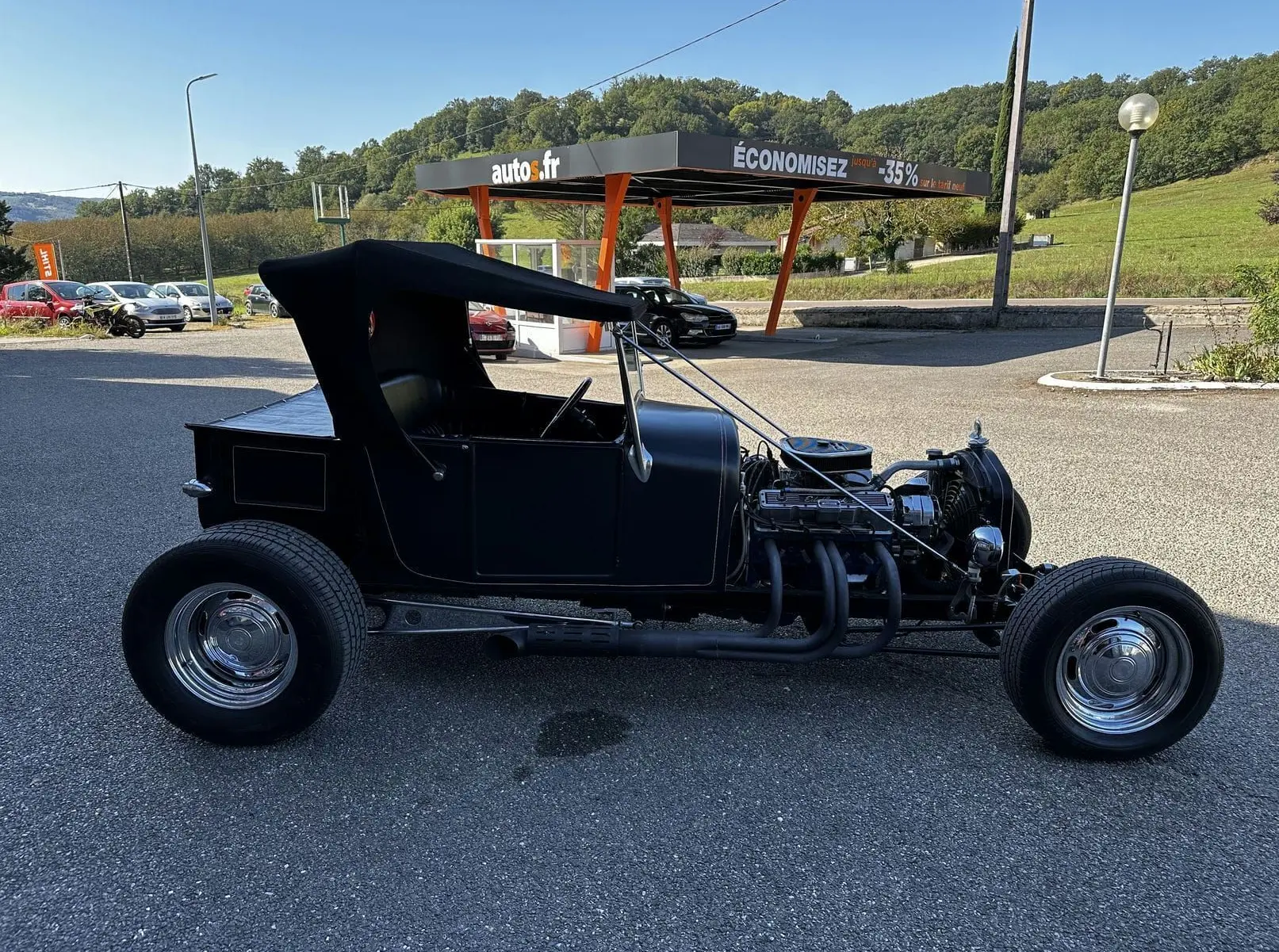 Profil côté gauche d'une Ford T Hot Rod V8 noire de 1923 avec toit décapotable en position haute et moteur apparent.