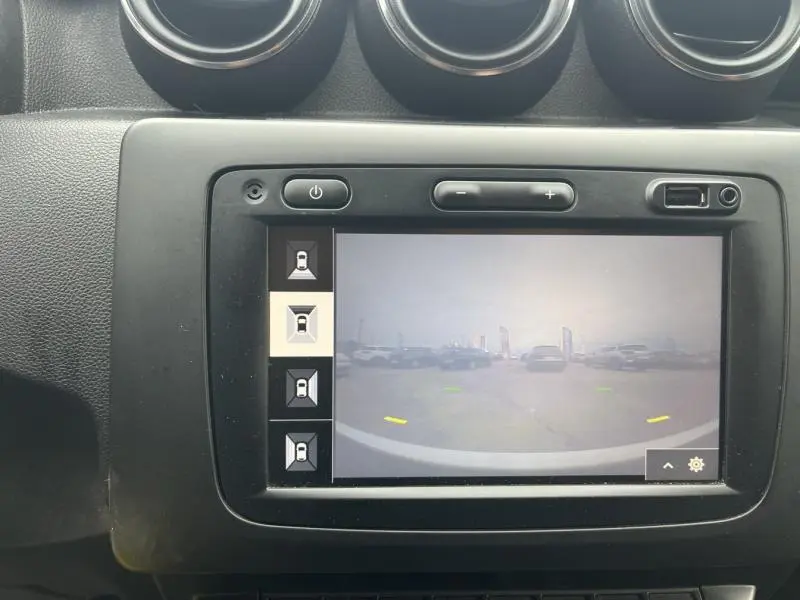 Écran tactile central affichant la caméra de recul du Dacia Duster blanc Glacier, vue arrière du parking visible.