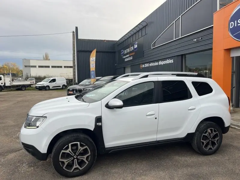 Profil côté gauche du Dacia Duster blanc Glacier 2019 avec jantes alliage et barres de toit chrome satiné.