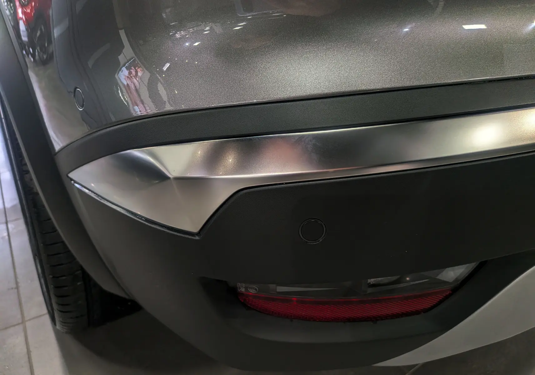 Gros plan sur le pare-chocs arrière gris Cassiopé du Renault Symbioz E-Tech, avec feu antibrouillard et capteur de recul visibles.